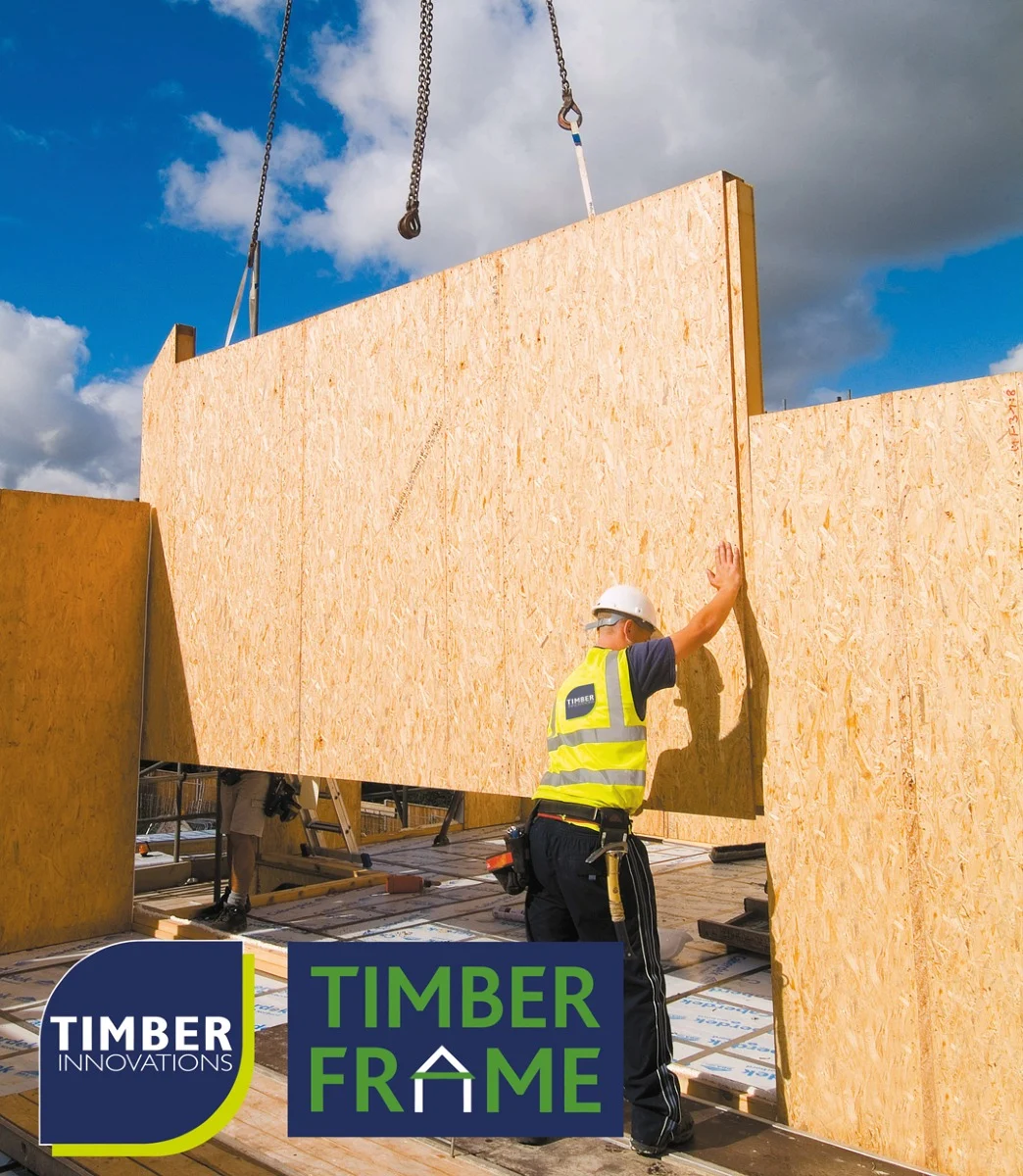 Man lowering a timber frame onto building site from crane