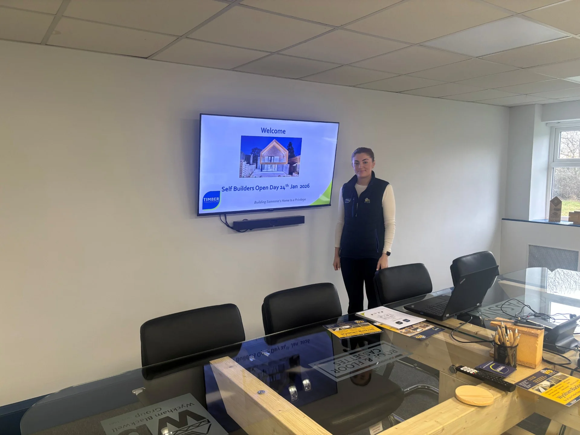 A lady standing in front of a screen with the Self Build Workshop details on a TV screen.