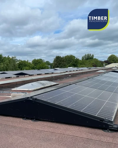 Rooftop solar panels on a flat commercial roof, cloudy sky; Timber Innovations logo in the top-right corner.